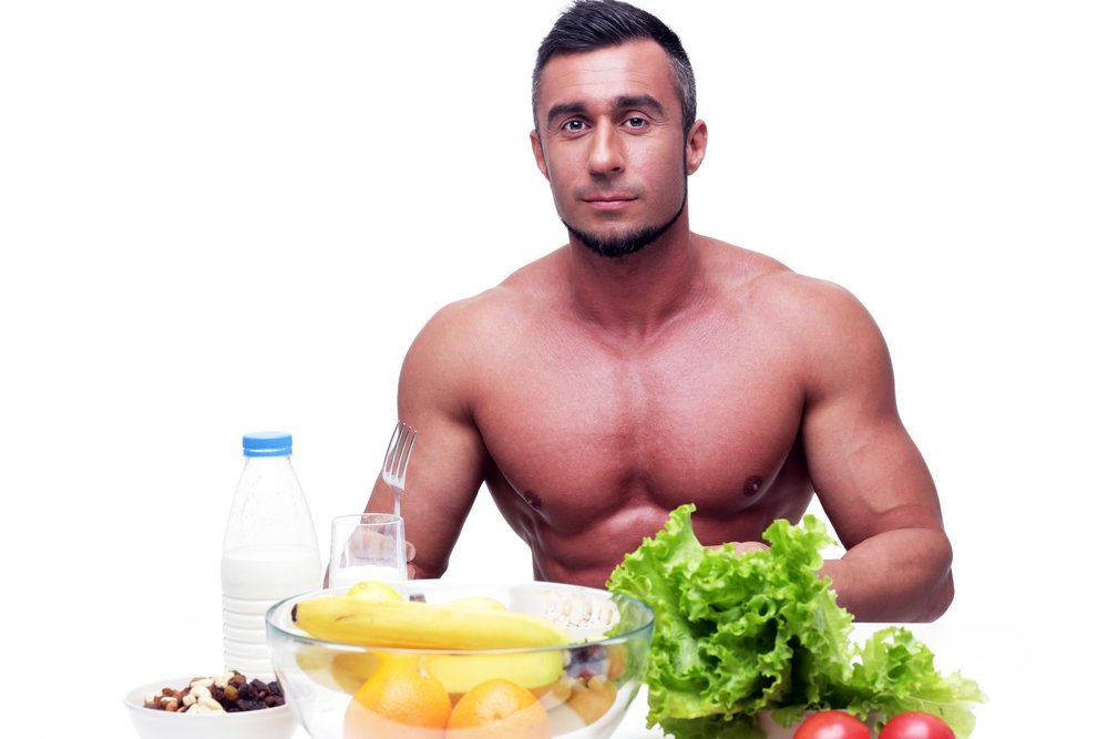 Handsome muscular man sitting at the table with healthy food